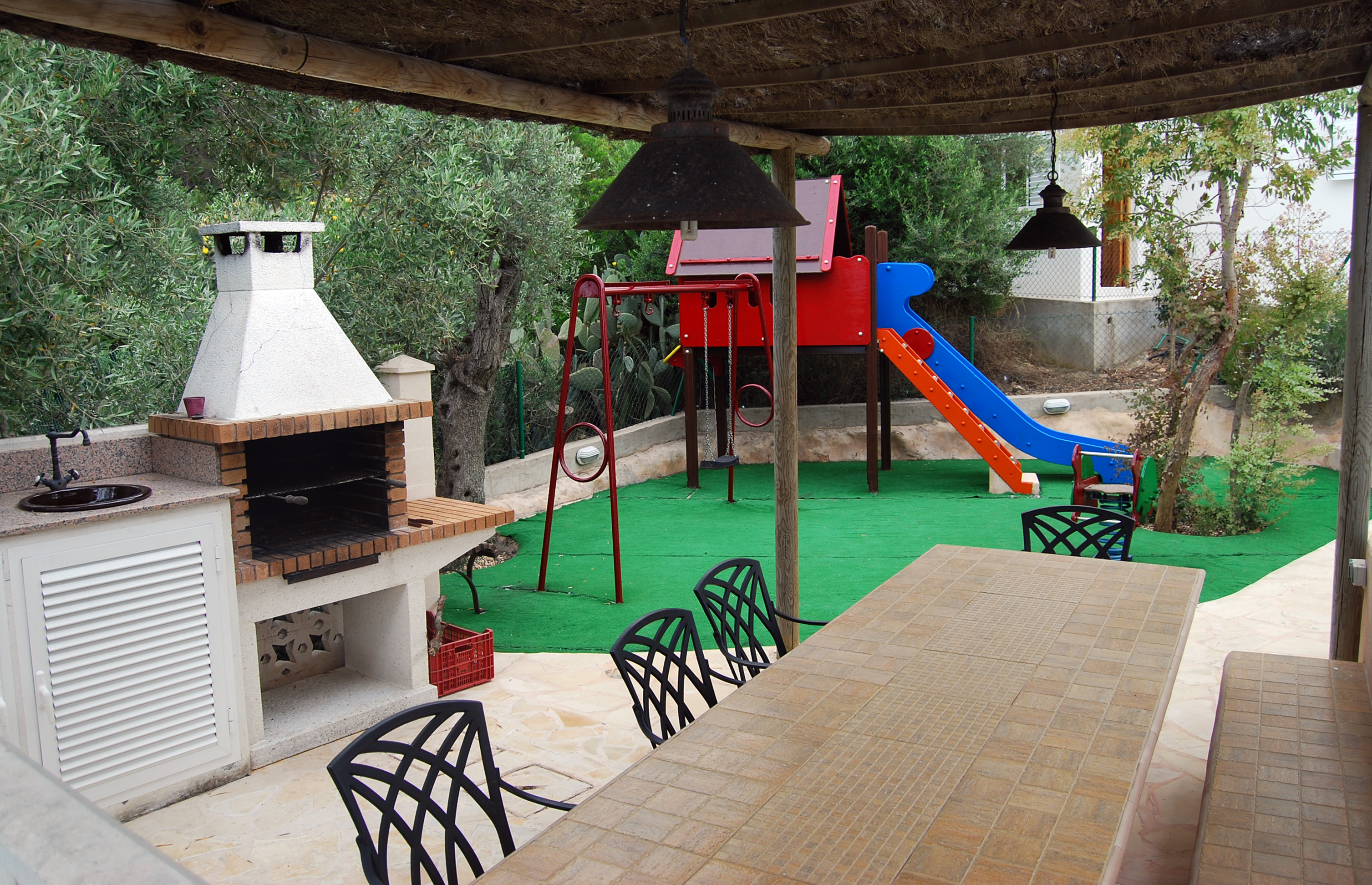 Outside dining table with barbecue next to a children's area